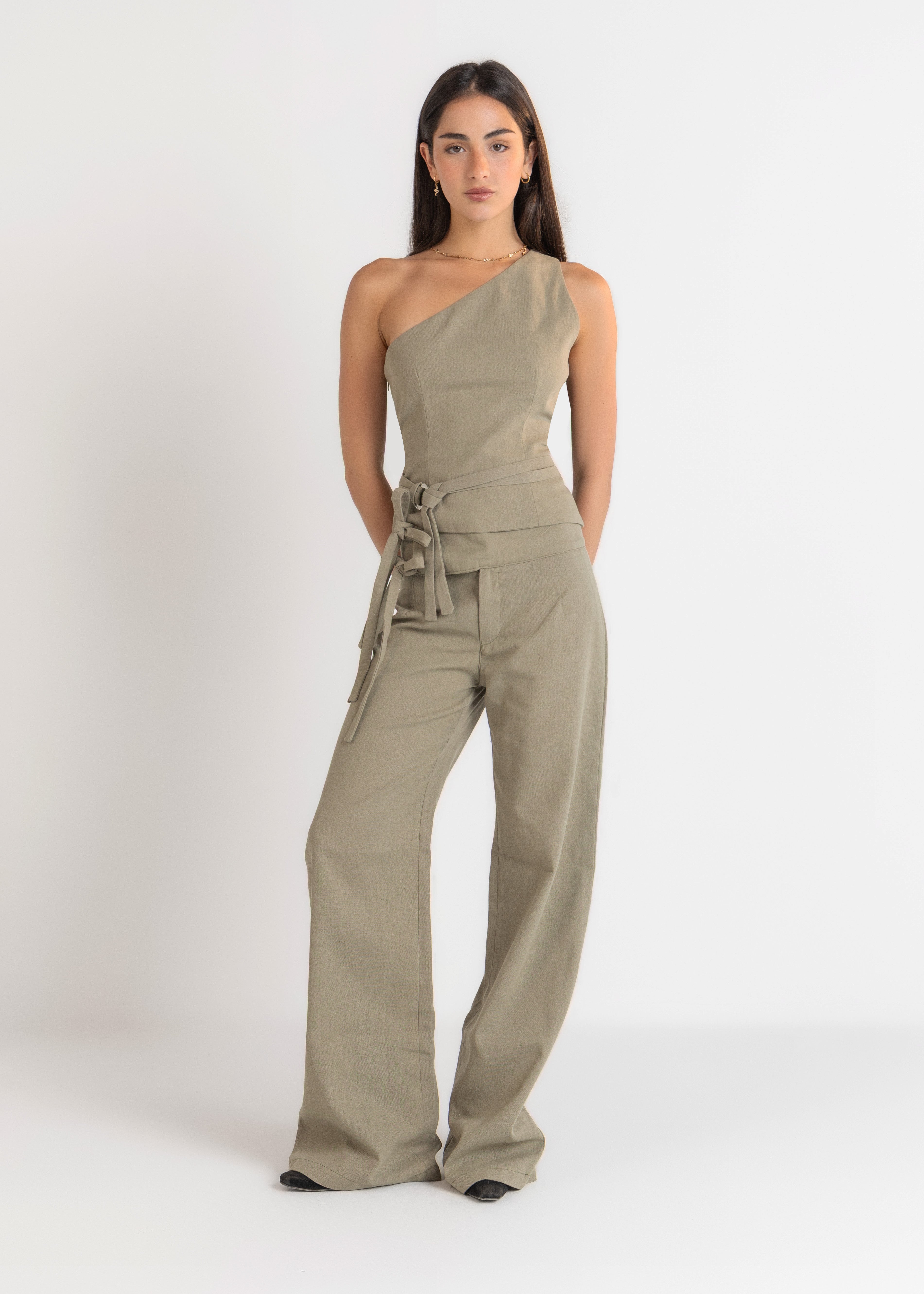 Woman wearing a khaki one-shoulder jumpsuit on a white background