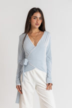 Woman wearing a light blue wrap top and white pants on a plain background