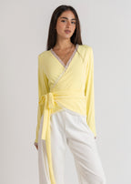 Woman wearing a yellow top and white pants on a light gray background