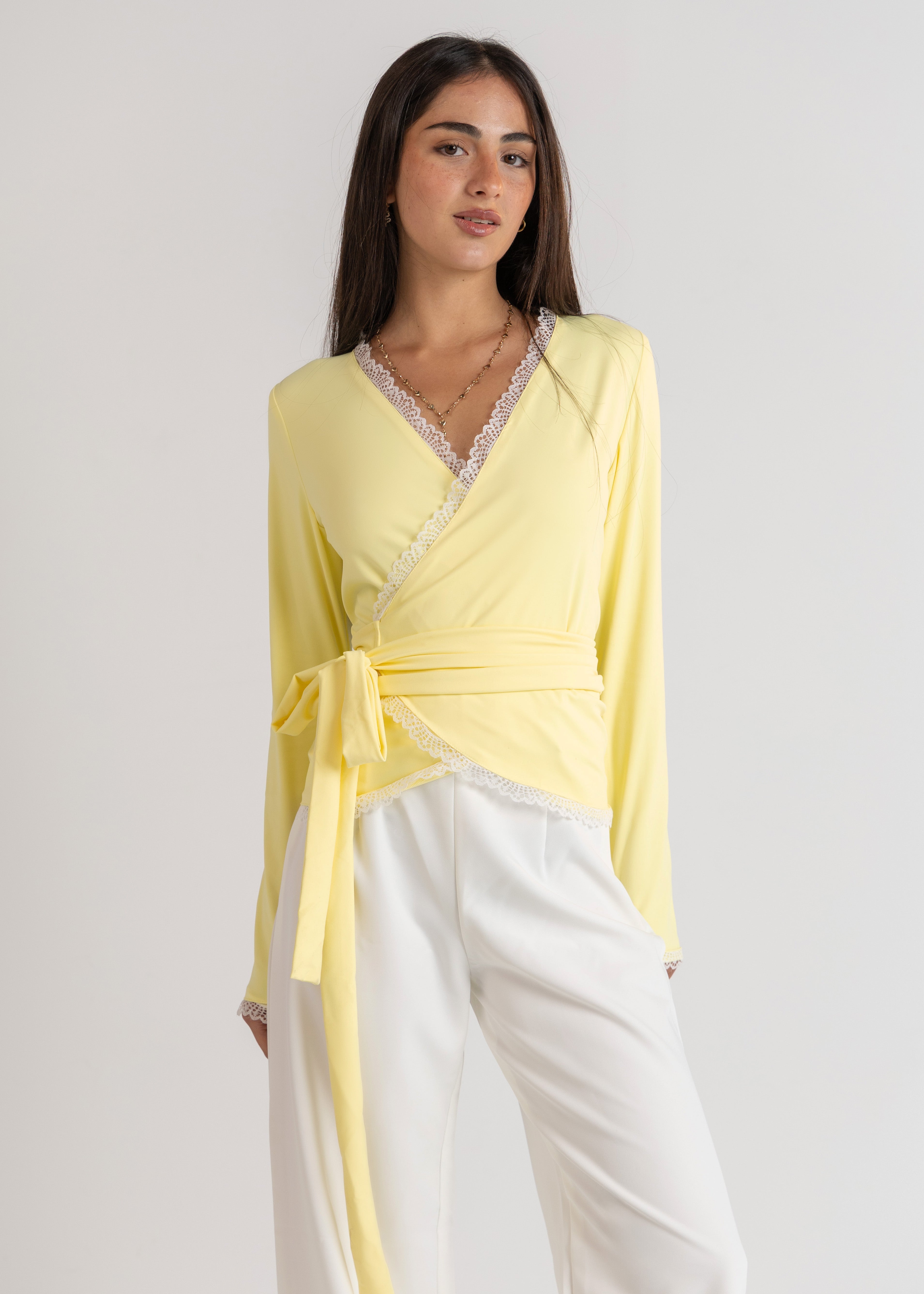 Woman wearing a yellow top and white pants on a light gray background