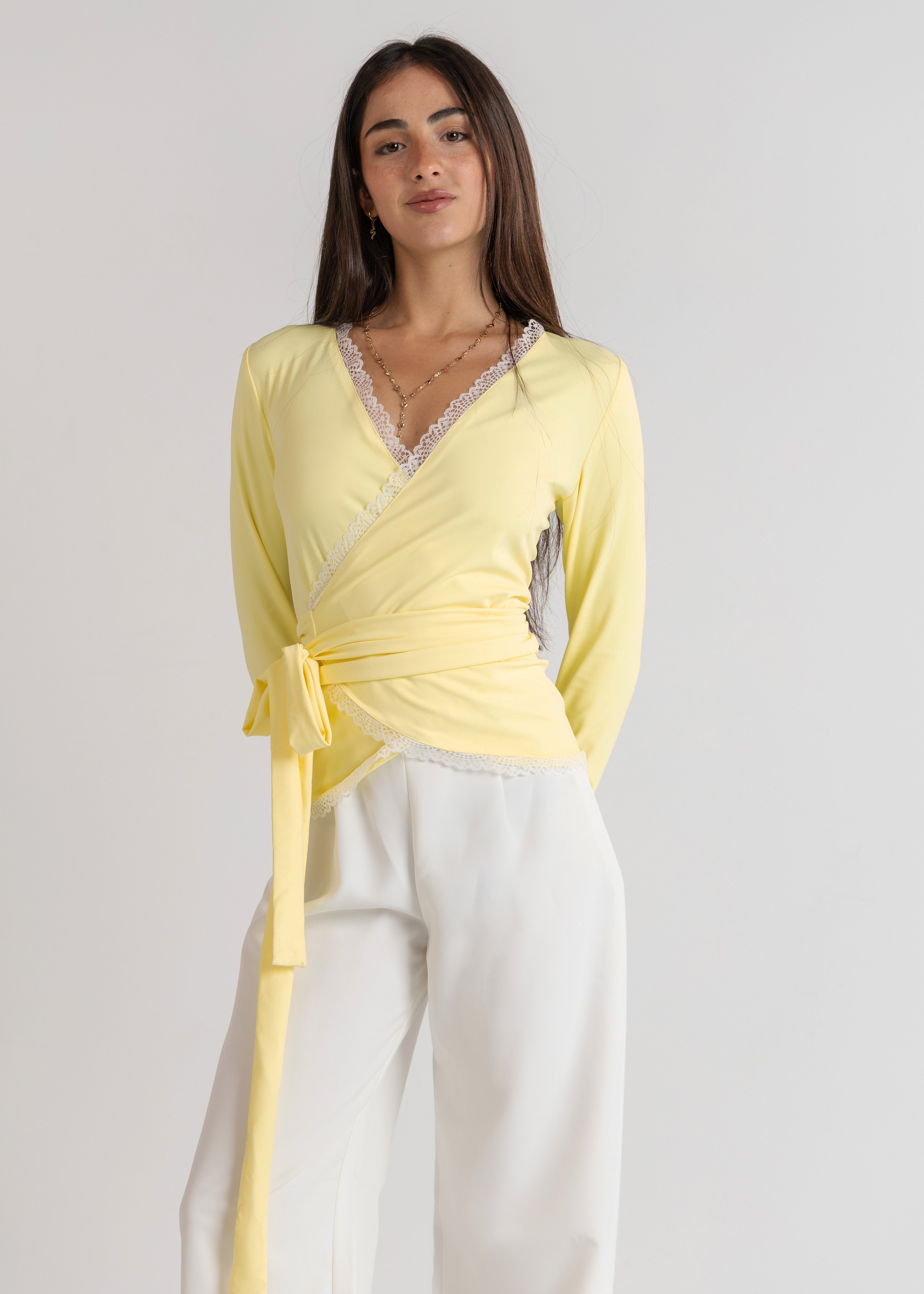 Woman wearing a yellow top and white pants against a plain background