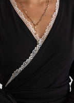 Black dress with lace detailing and a necklace on a neutral background