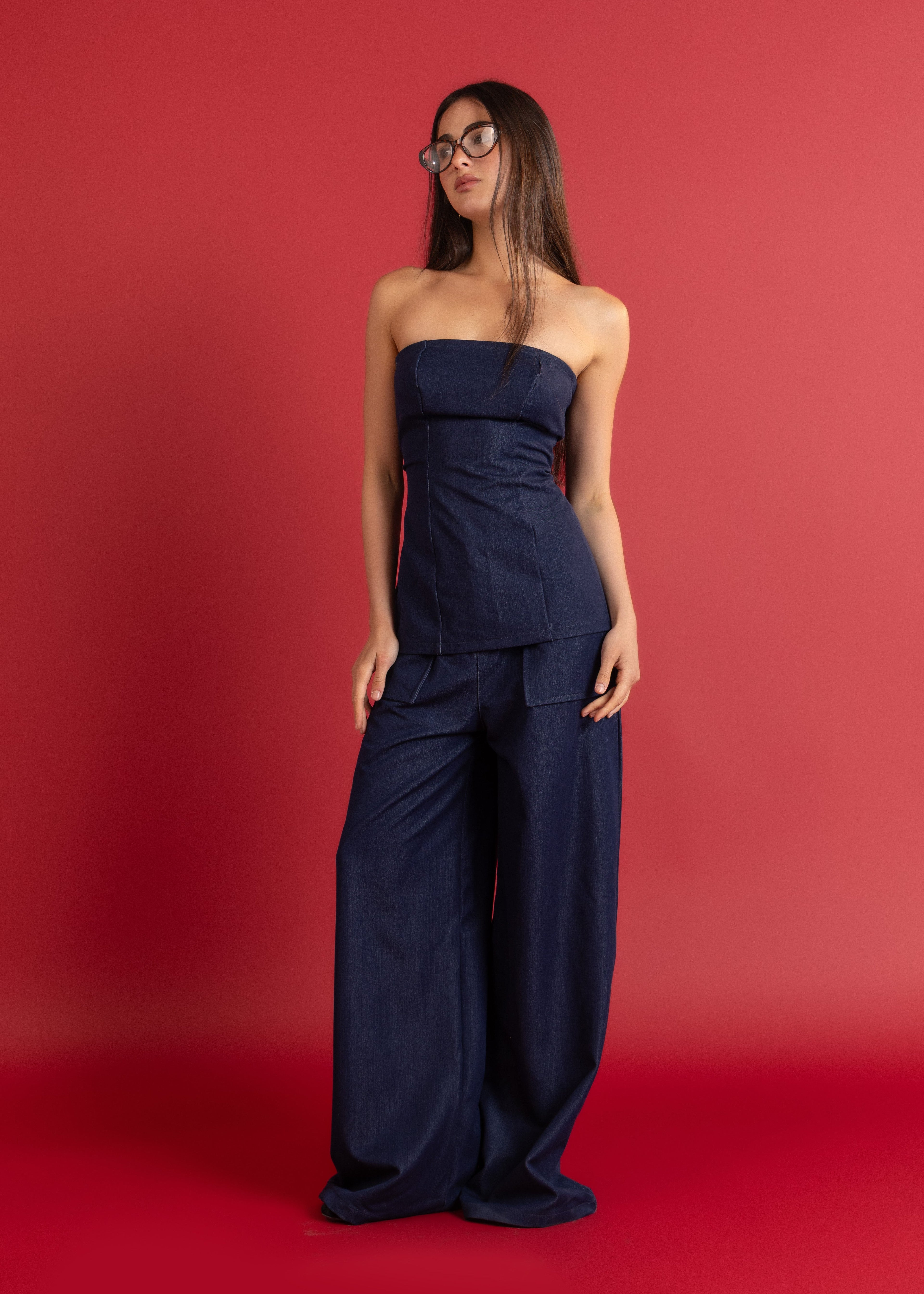 Woman wearing a navy strapless top and wide-leg pants against a red background