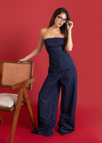 Woman in a strapless navy jumpsuit standing against a red background