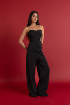 Woman wearing a black strapless top and wide-leg pants against a red background