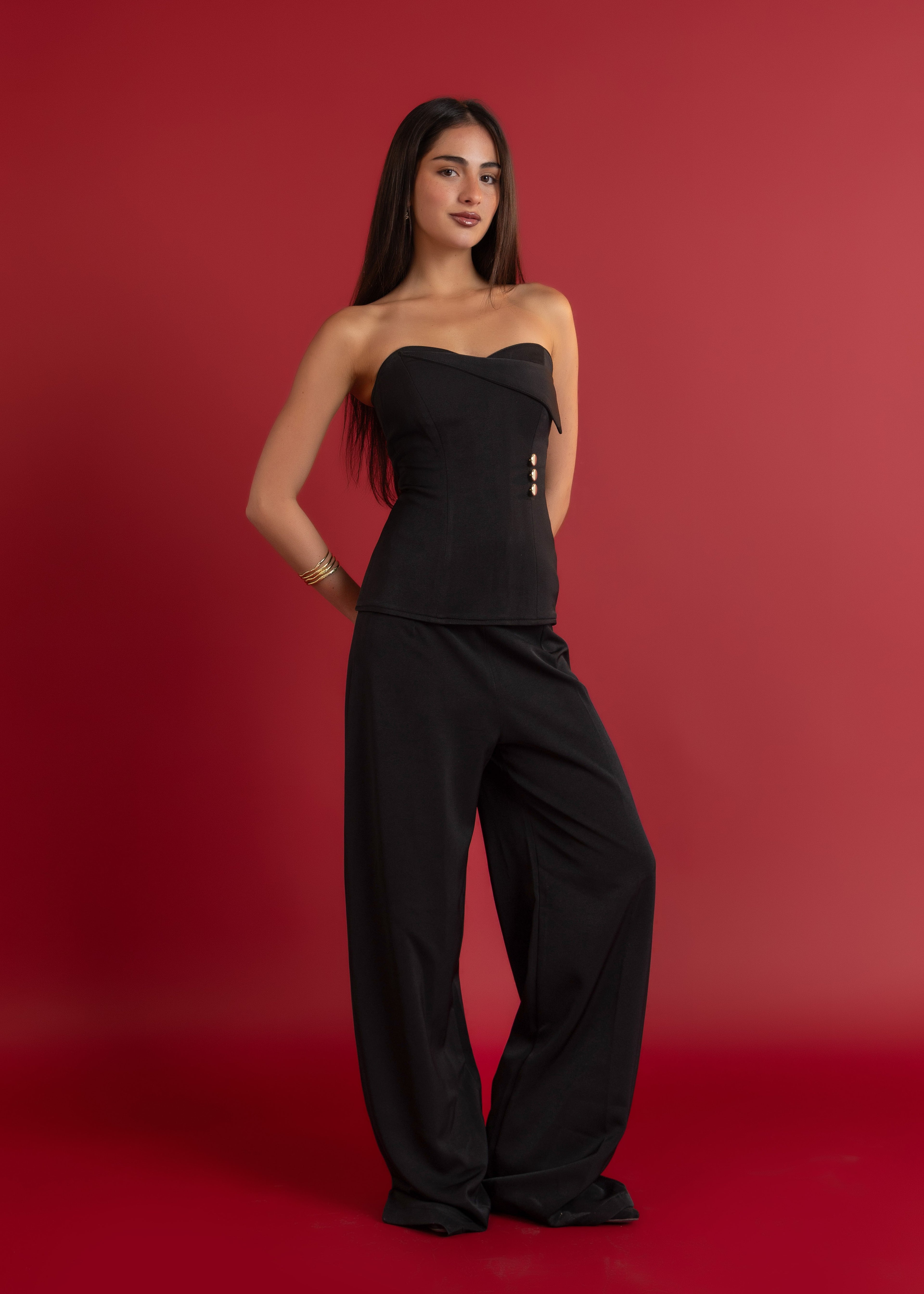 Woman wearing a black strapless top and wide-leg pants against a red background