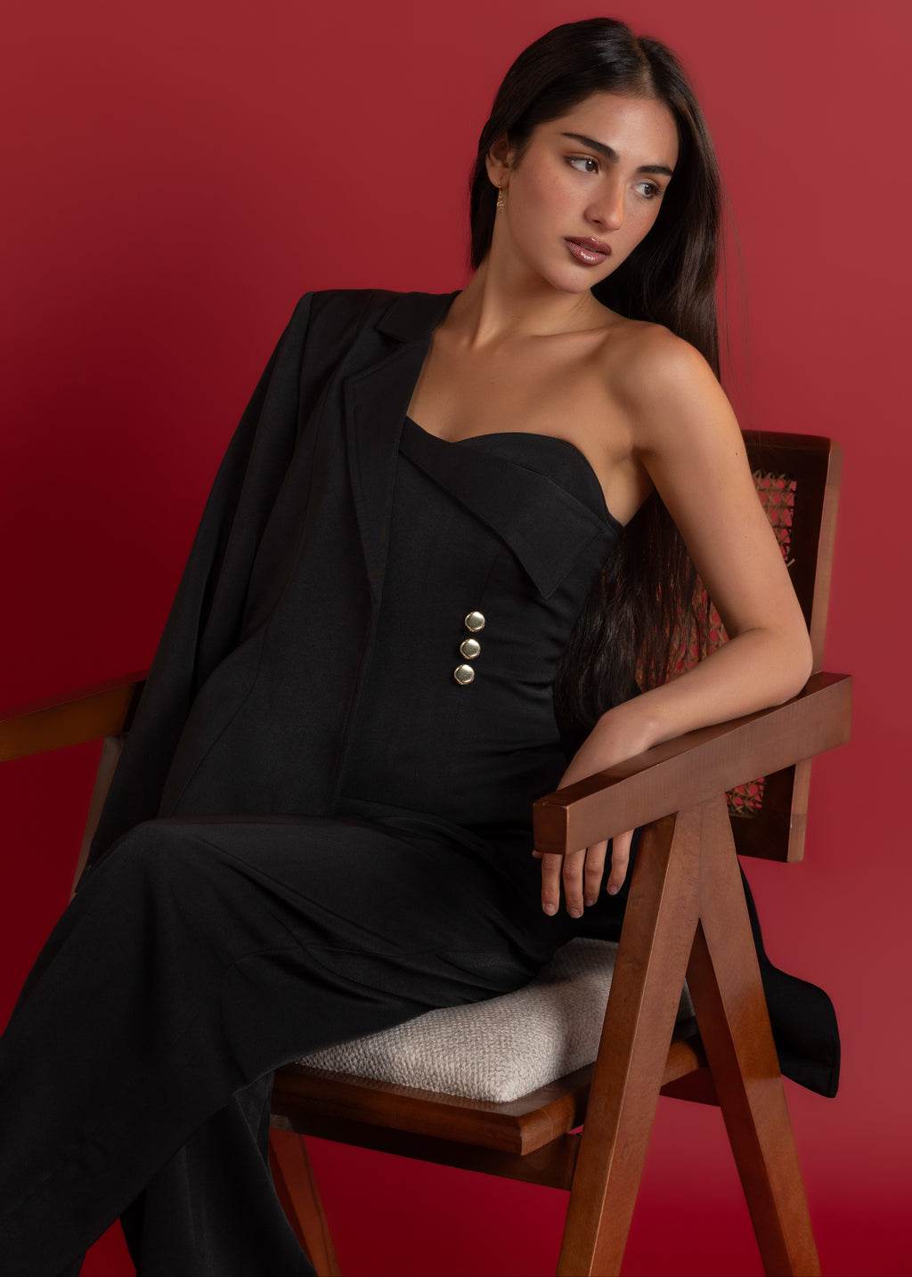Woman in a black dress sitting on a wooden chair against a red background