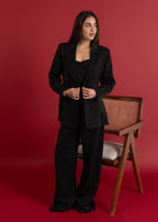 Woman in a black suit standing against a red background with a chair visible.
