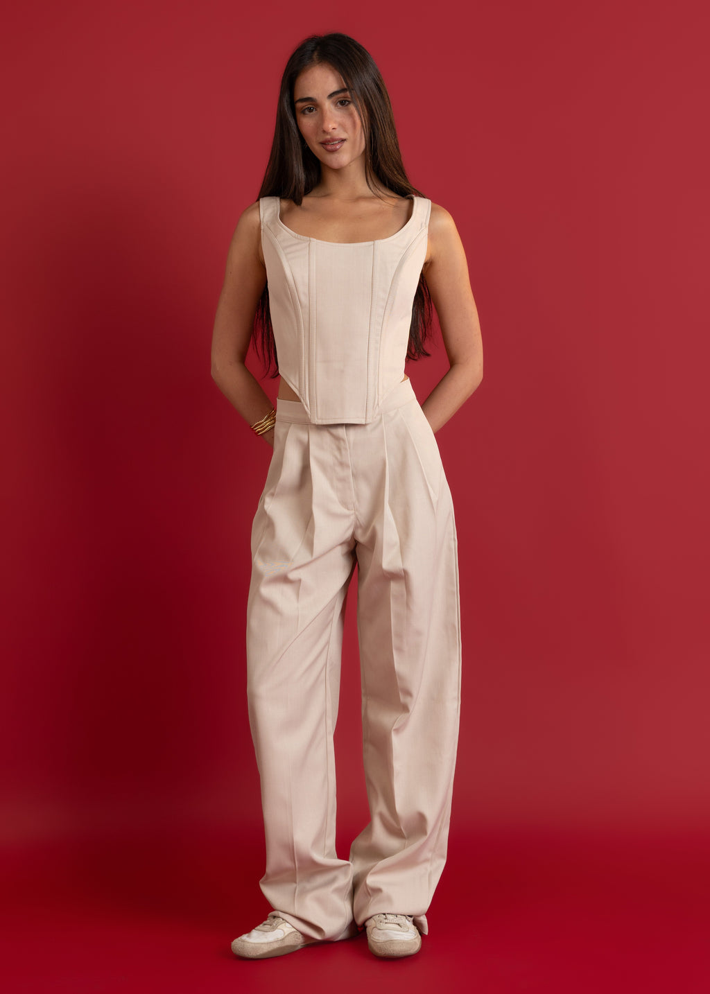 Woman wearing a beige sleeveless top and pants against a red background
