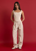 Woman wearing a beige sleeveless top and pants against a red background