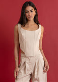 Woman wearing a beige sleeveless top and pants against a red background