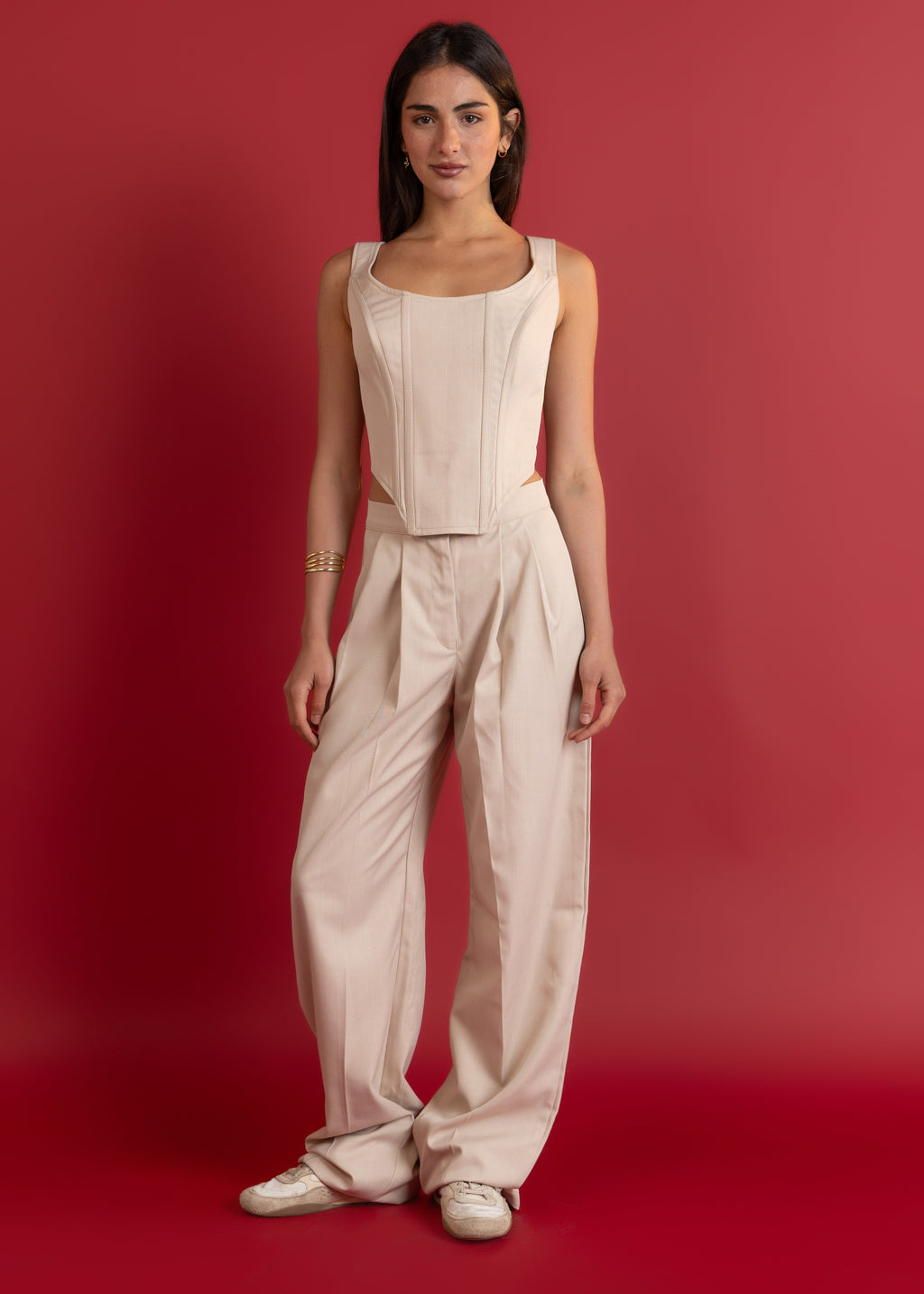 Woman wearing a beige sleeveless top and pants against a red background