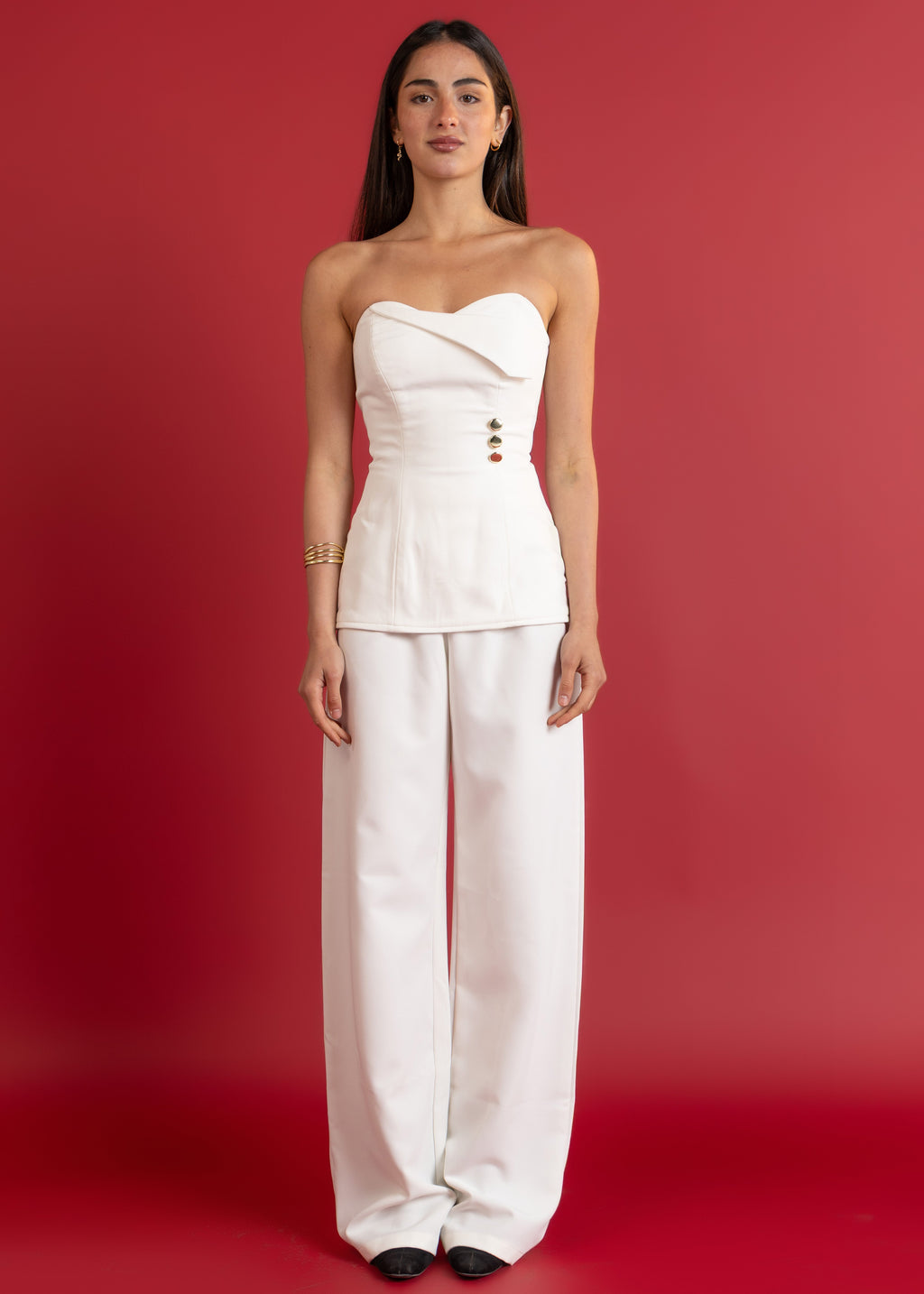 Woman wearing a white strapless top and wide-leg pants against a red background