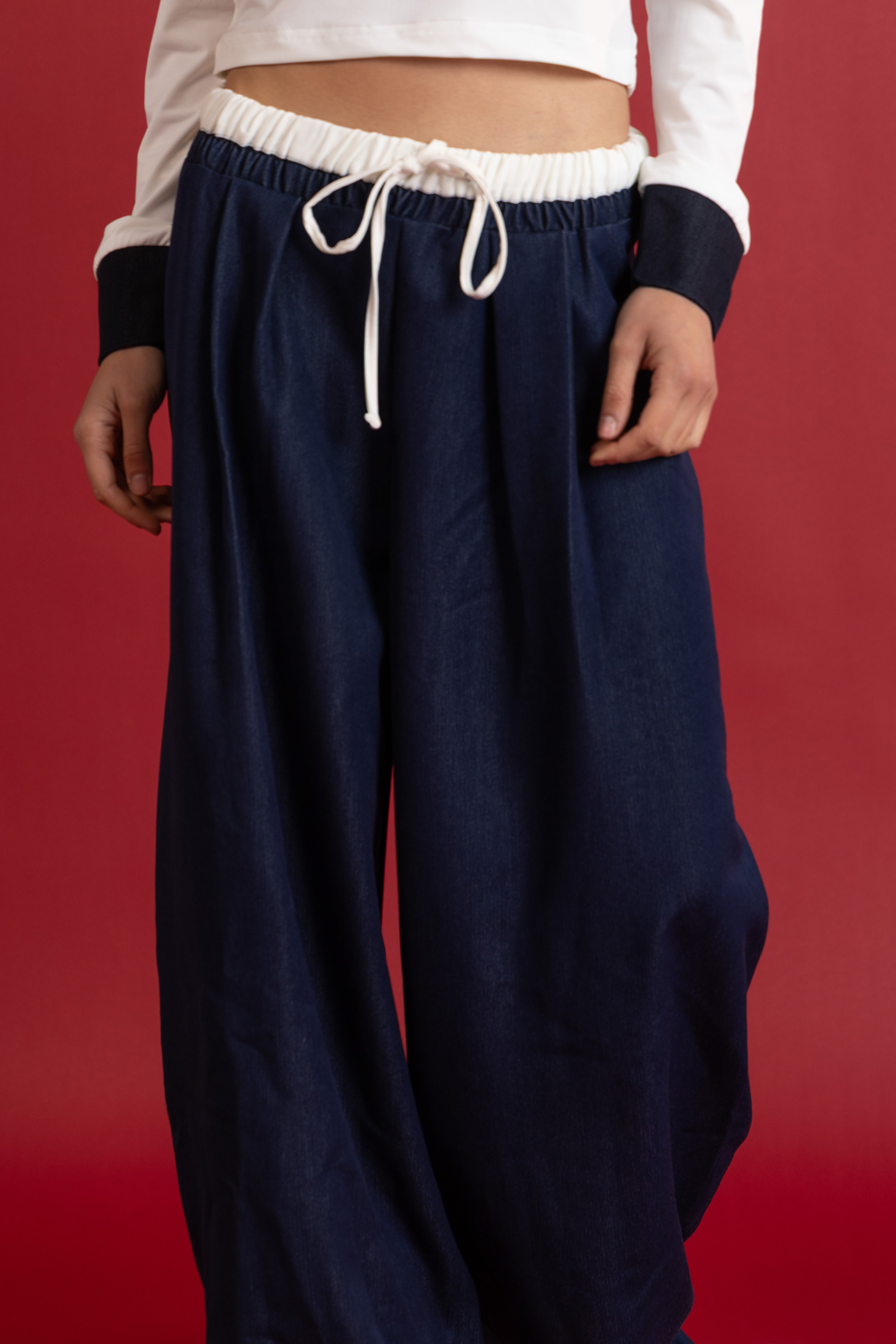 Person wearing navy blue pants with a white top on a red background